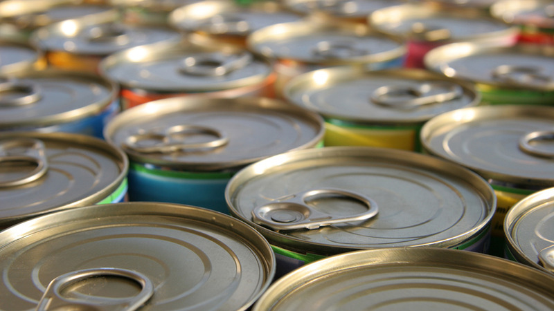 Close-up view of several metal cans with pull-tab lids arranged in rows, showing the tops of the cans with tabs in various orientations and faint label colors around the edges.